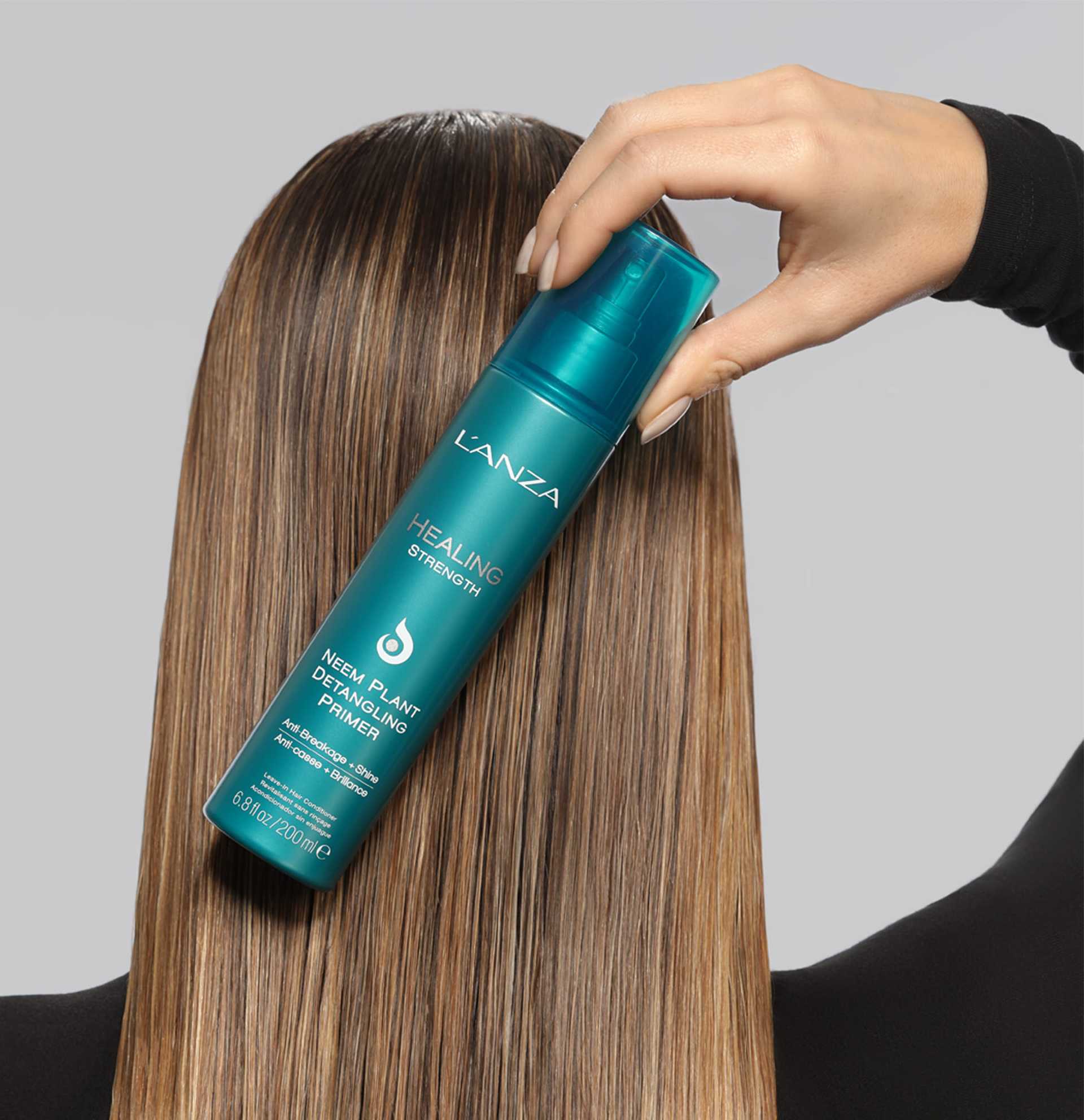 Hair product applied to long, straight hair by hand; teal spray bottle labeled L'ANZA Healing.