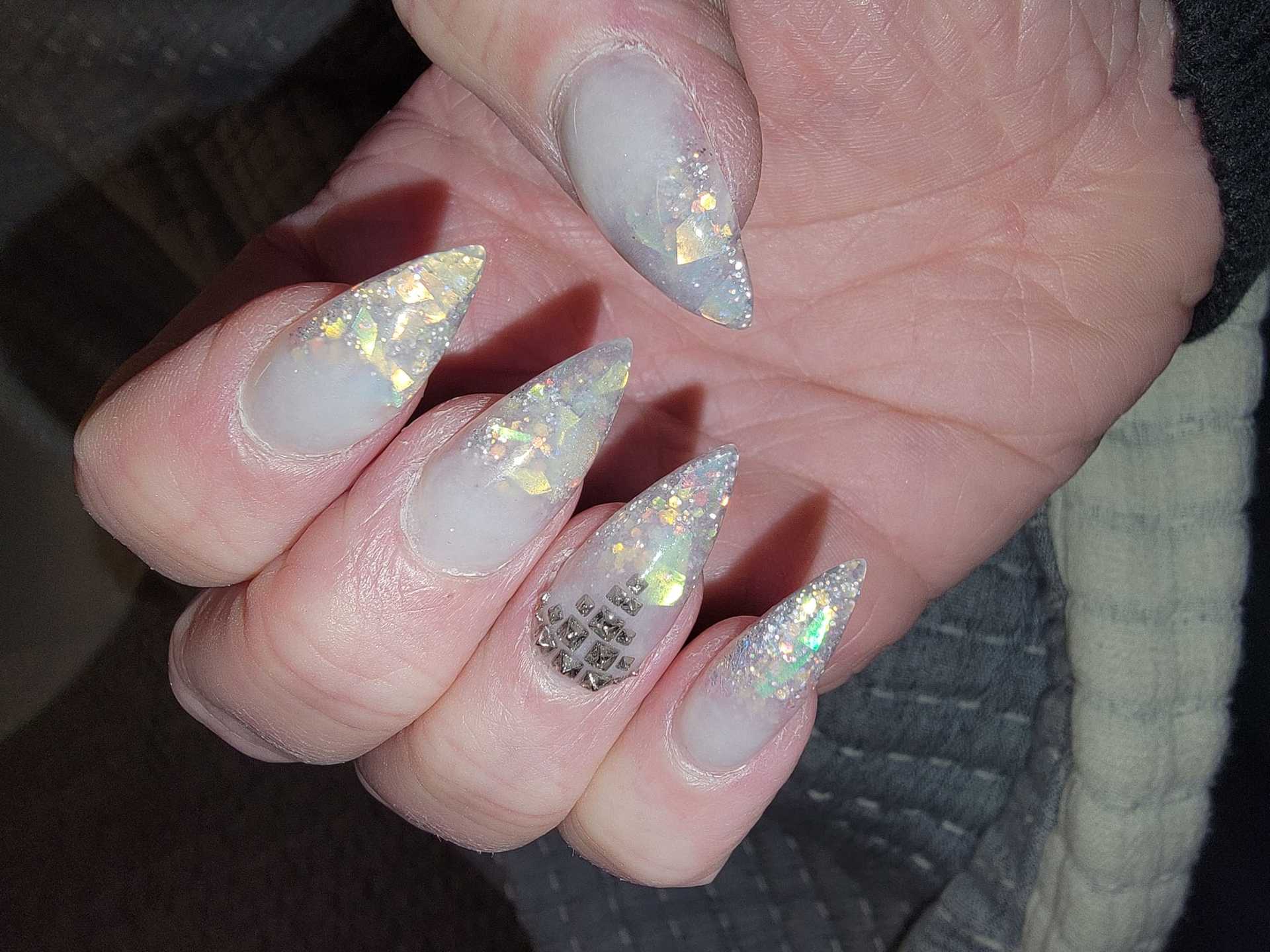 Sparkling stiletto nails with glitter and gem accents on one finger.