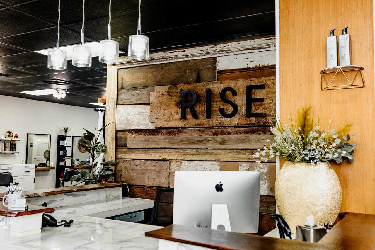 Salon reception area with wooden decor and "RISE" sign behind the desk.