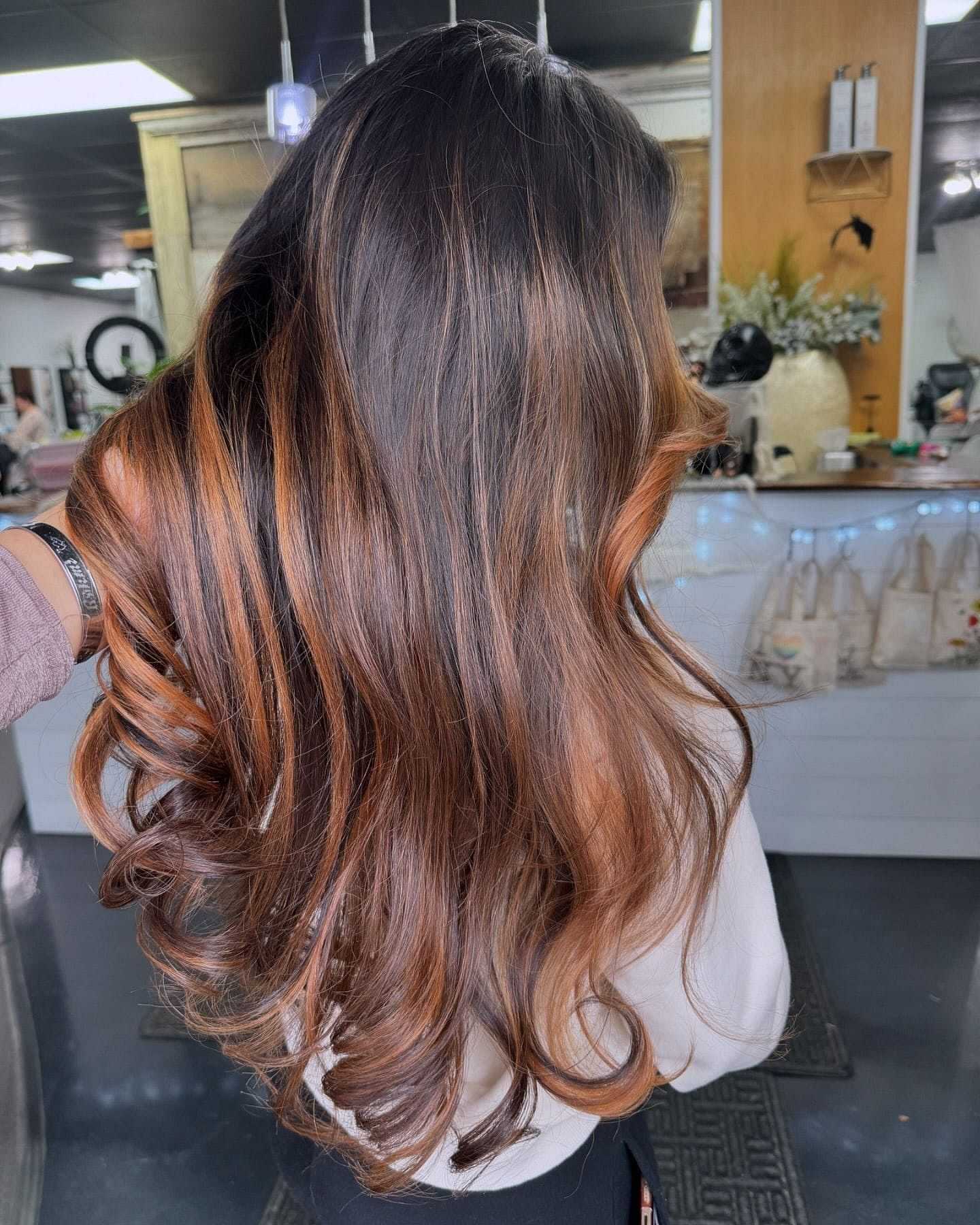 Luxurious, wavy brunette hair with caramel highlights in a salon setting.