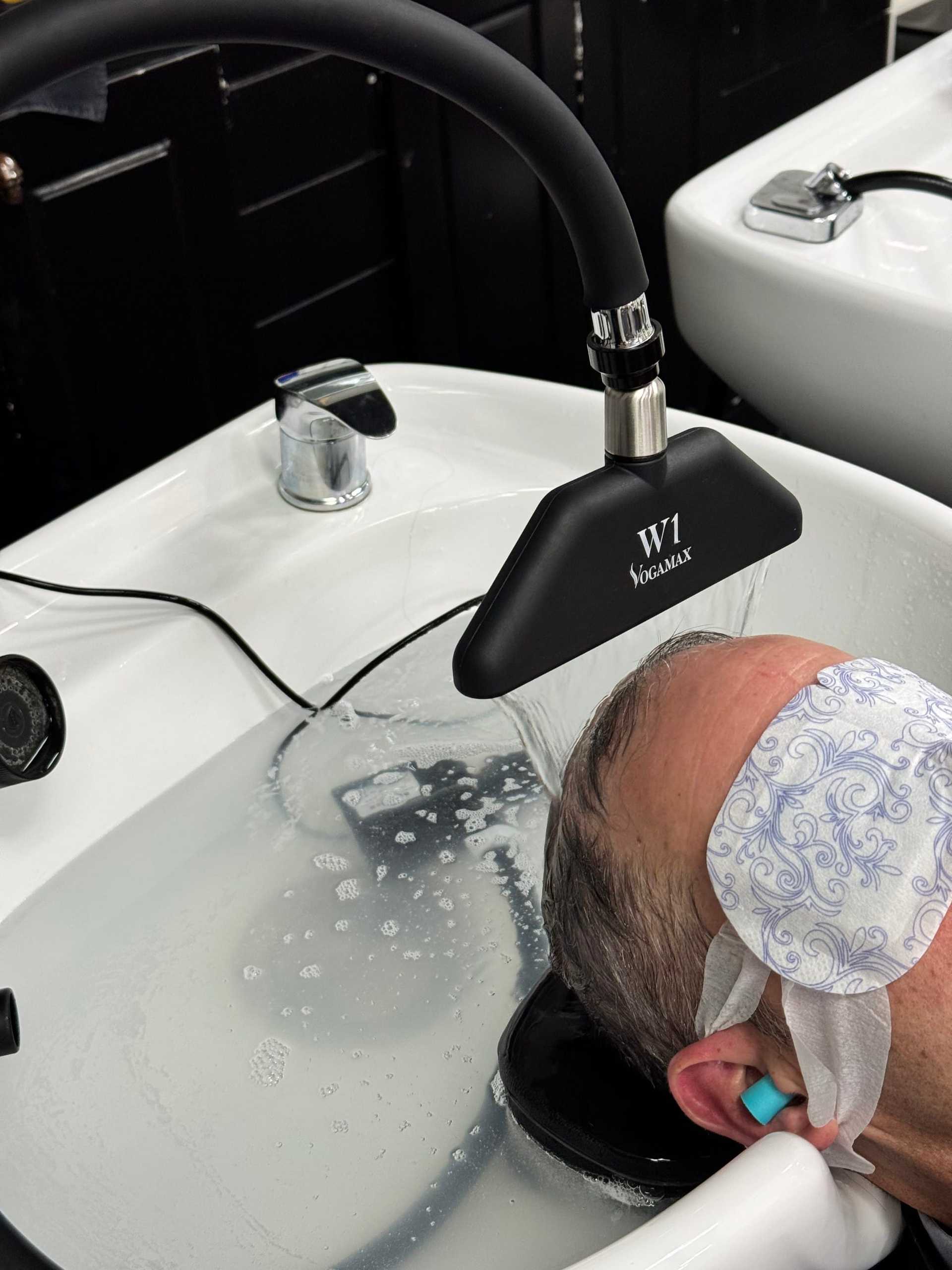 Man with eye mask getting hair washed at salon sink.